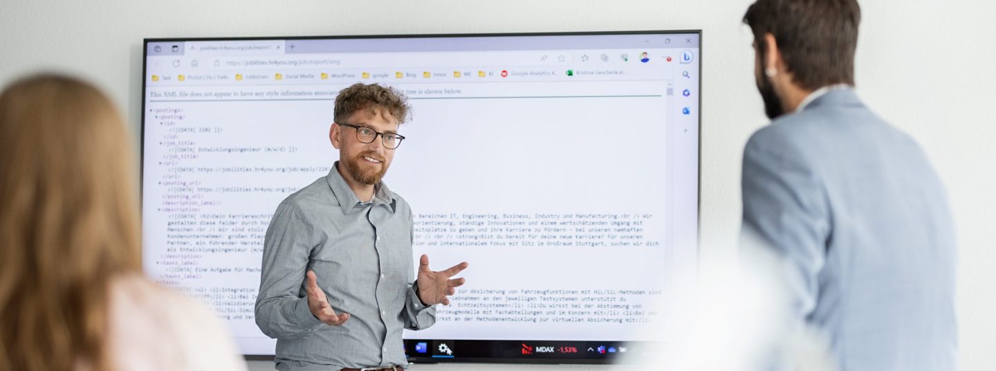 Ein Mitarbeitender der AutoVision hält eine Präsentation vor einem Smartboard, auf dem ein Programmcode zu sehen ist.