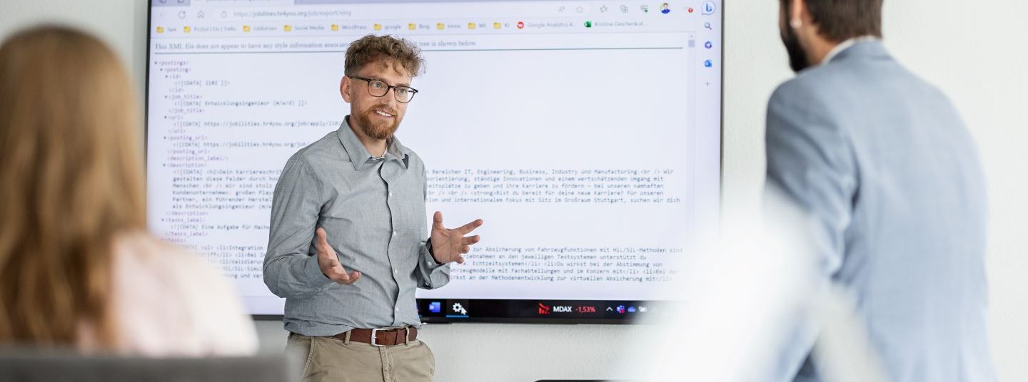 Mitarbeiter der AutoVision hält eine Präsentation. Im Hintergrund ist ein großer Bildschirm, auf dem ein Programmcode zu sehen ist.