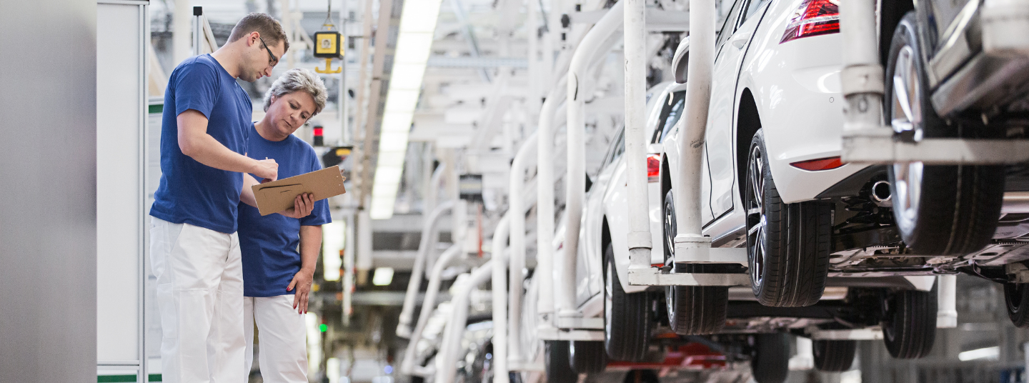 Zwei Produktionsmitarbeitende in Arbeitskleidung an der Fertigungslinie im Volkswagen Werk Wolfsburg.